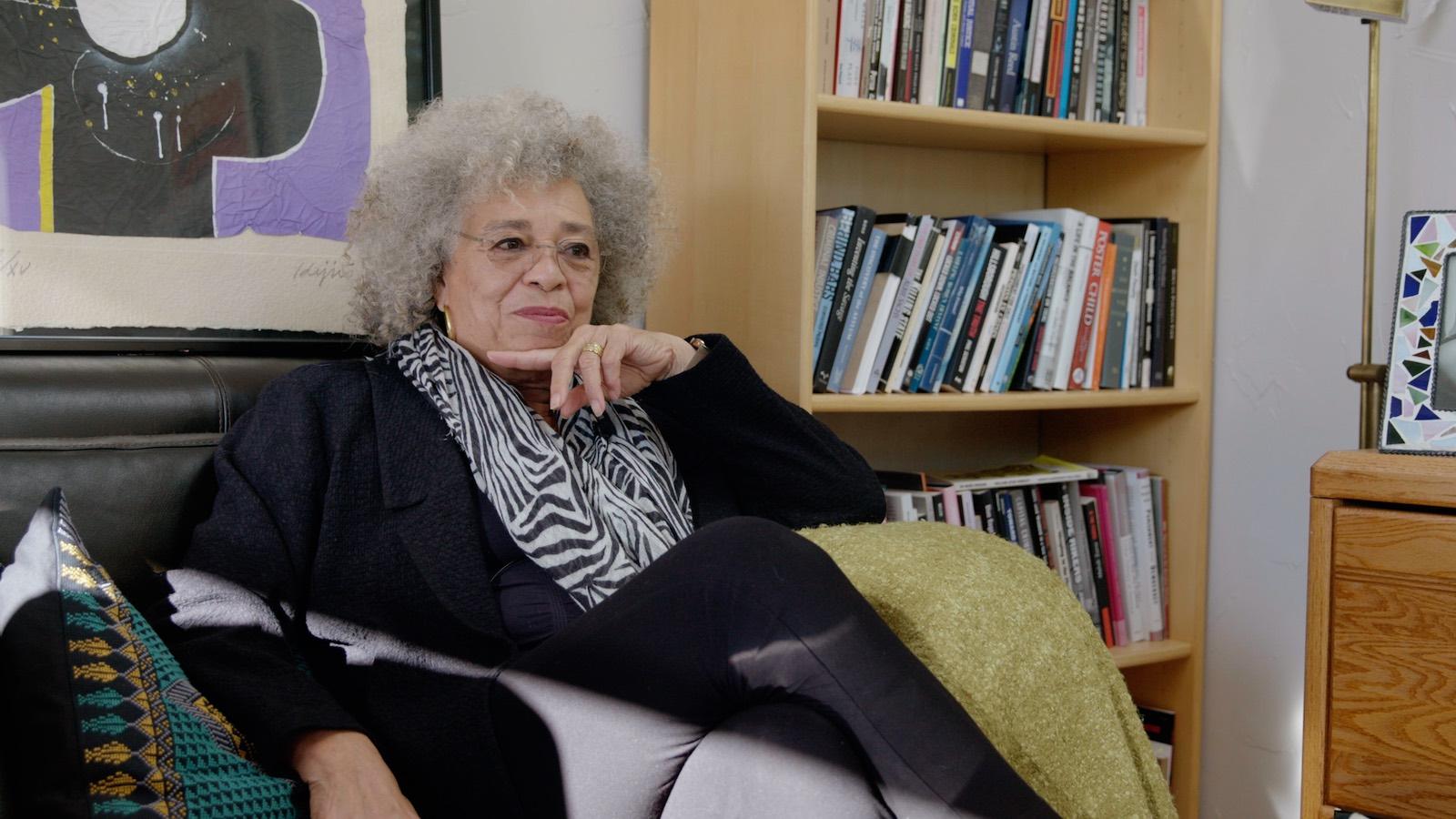 Angela Davis seated in interior shot, next to bookcase